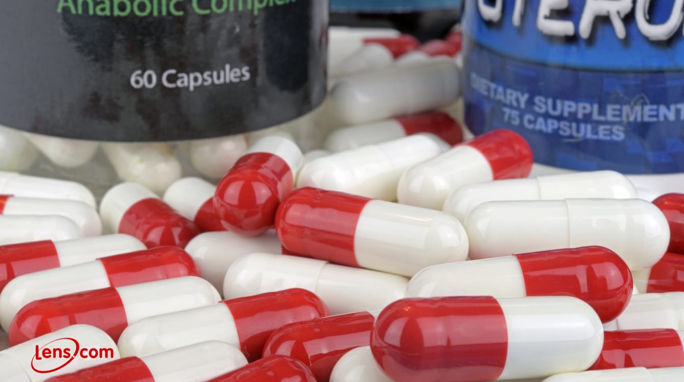ed and white capsules piled near supplement bottles labeled anabolic complex and steroids.