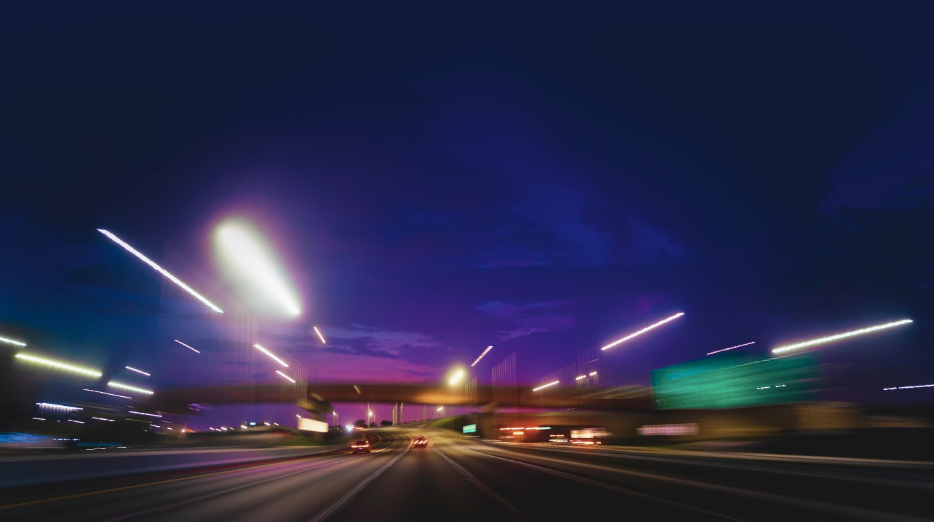 Streaked and blurred highway lights captured from a moving vehicle on a dark evening drive.