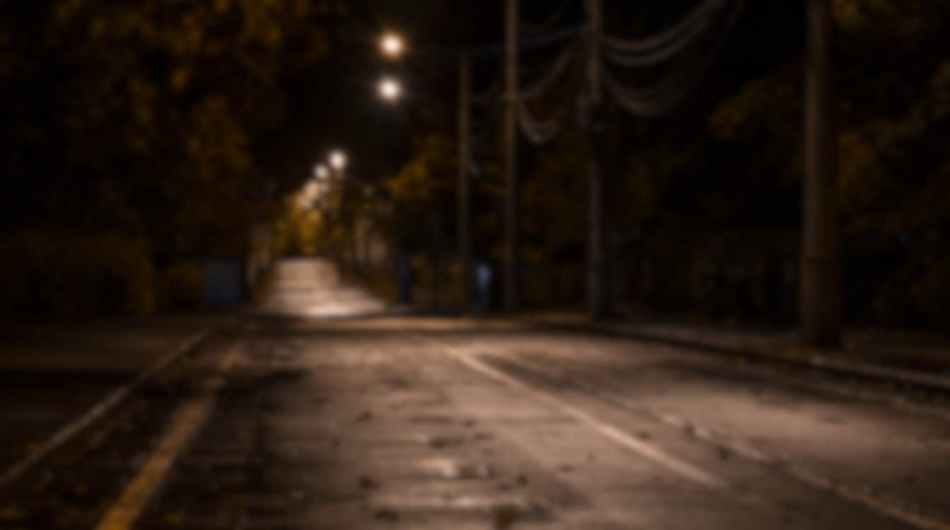 A quiet street at night with blurred lamps and low contrast, creating a hazy view of the road.