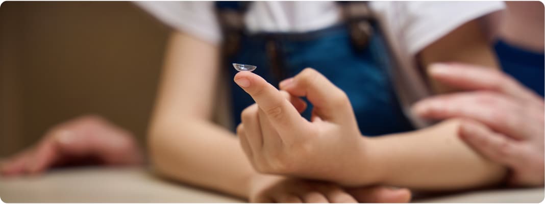A child holding a contact lens whilst a parent watches over them