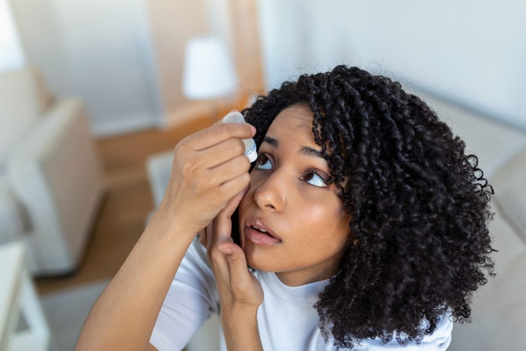 woman putting eye drops to clear contact lenses debris
