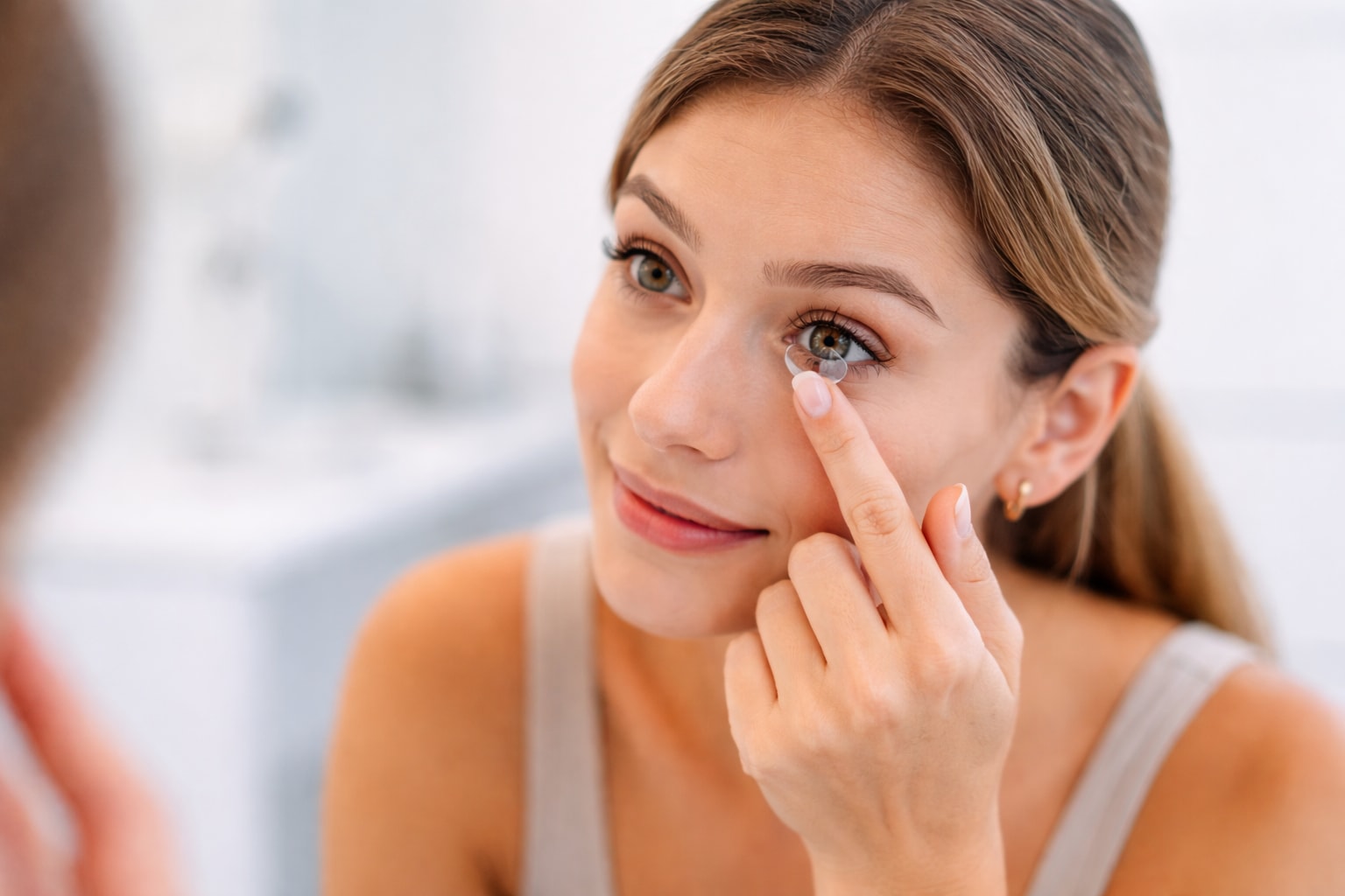 Woman inserting a contact lens into her eye while looking in a mirror.