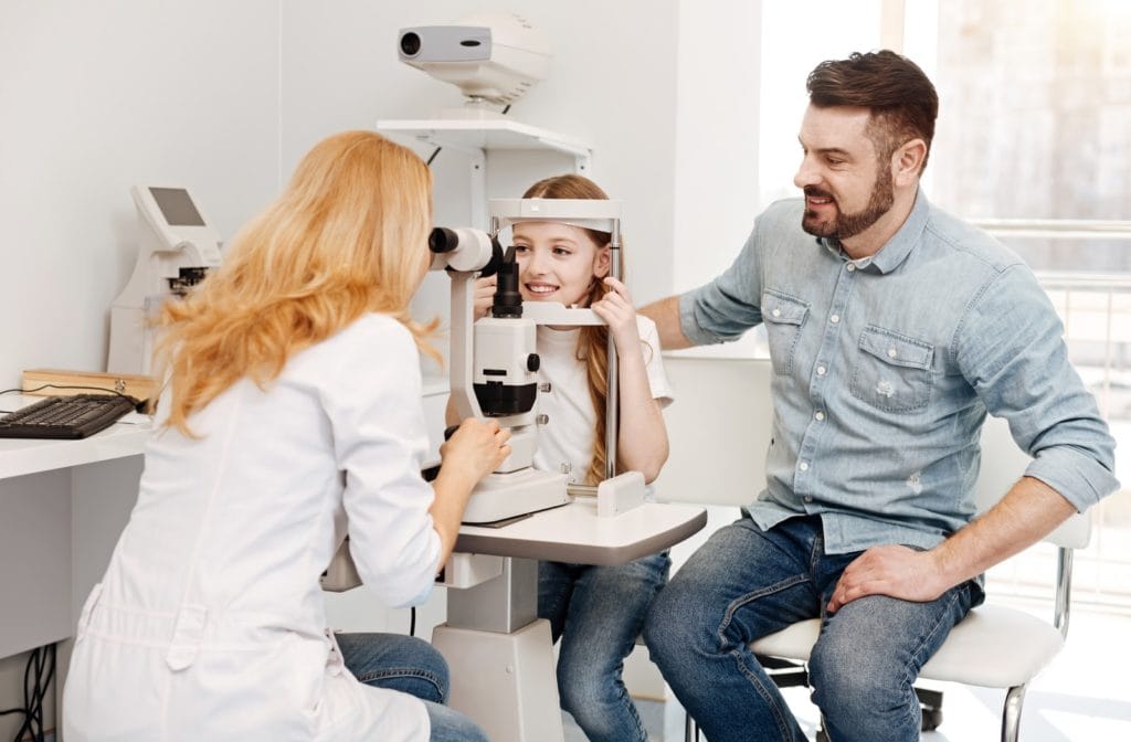 Warning Signs Your Child May Have a Vision Problem: child getting an eye exam in a clinic while a parent sits nearby.