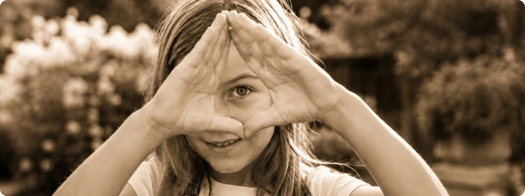Child in a garden using her hands to frame one eye, illustrating a simple dominant eye test in a sepia photo style.