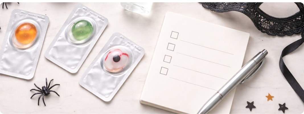 Flat lay of colored contact lens supplies with a lens case and solution beside small Halloween accents.