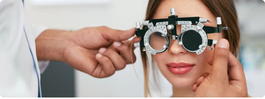 Patient taking a vision test as an optometrist adjusts a phoropter in a clinic exam room.
