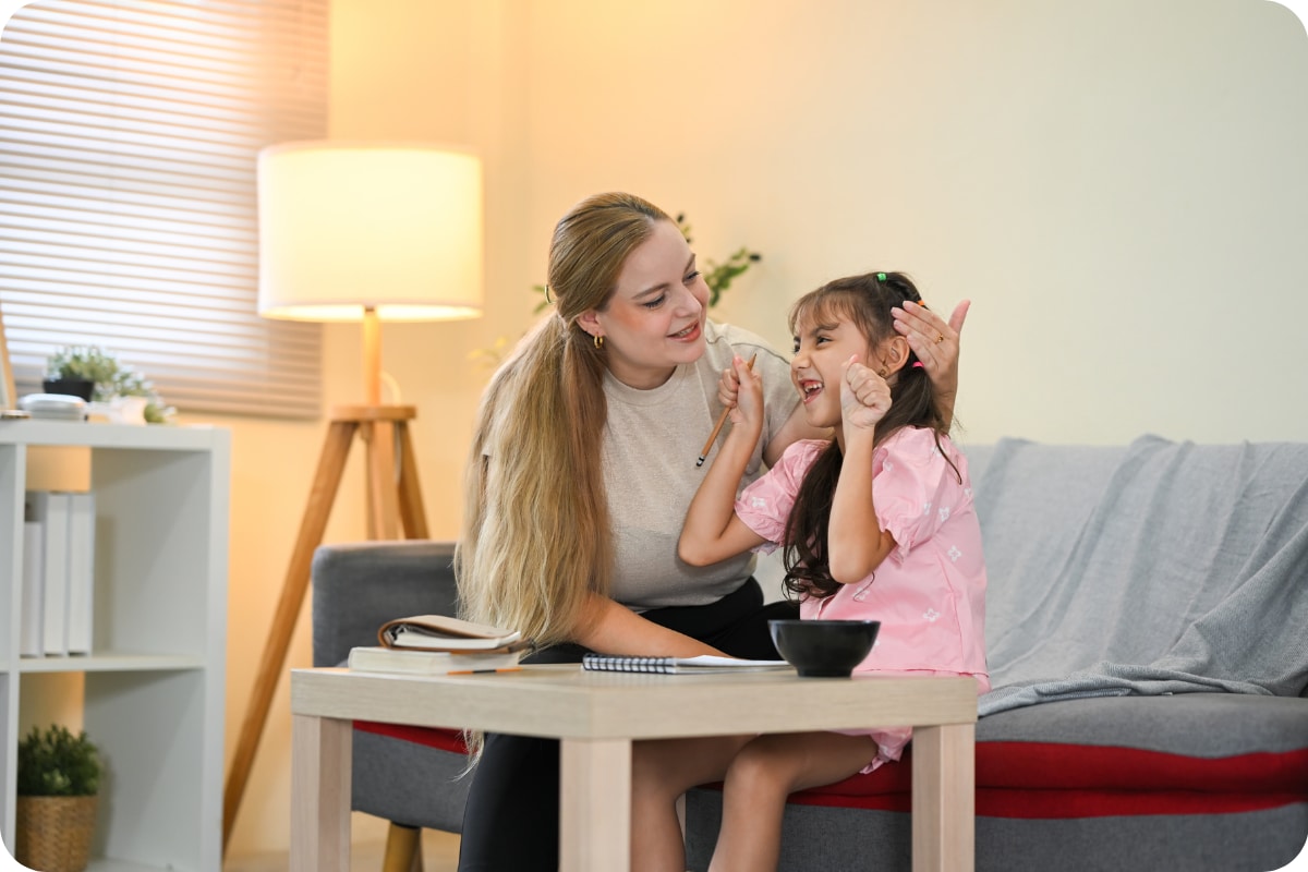 Parent helping a young child practice a task at home while sitting together on a couch.