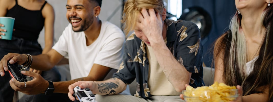 Group of friends playing video games together indoors with controllers and snacks.