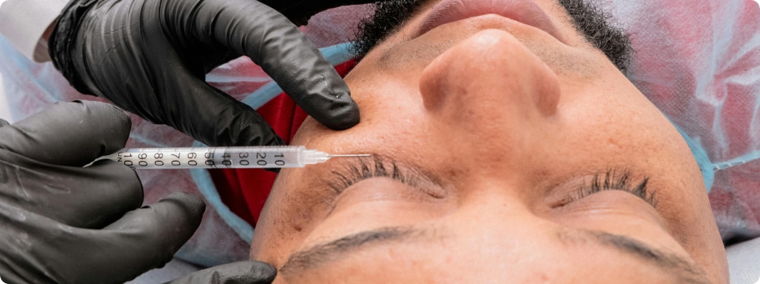 A plastic surgeon injecting botox under the eye of a patient.